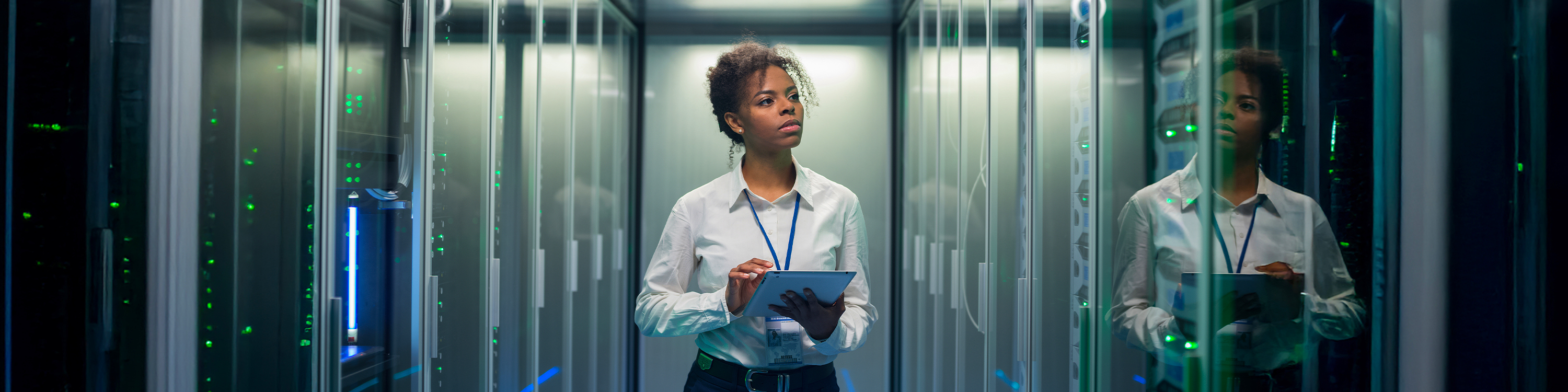 A woman in a business suit stands confidently in a server room filled with rows of servers and blinking lights.