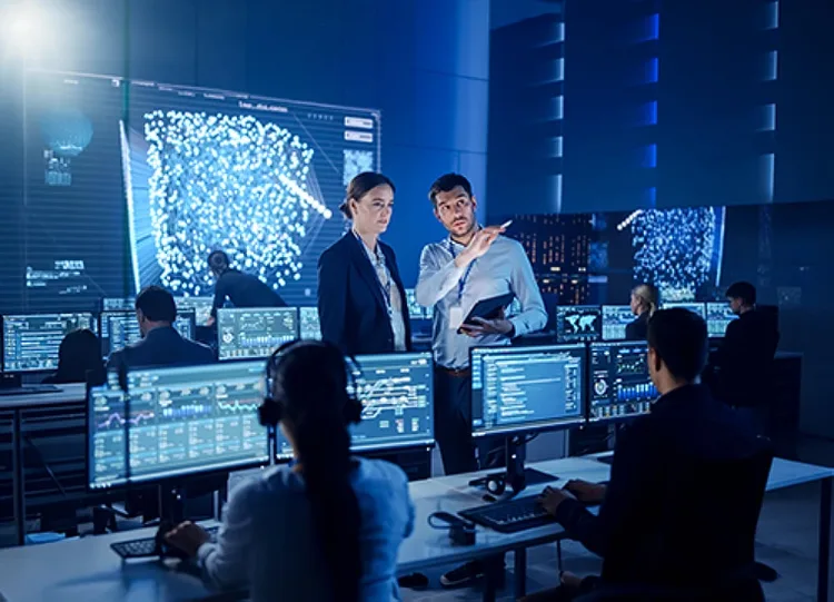 A group of people working in a control room with multiple monitor screens and a large screen at the front