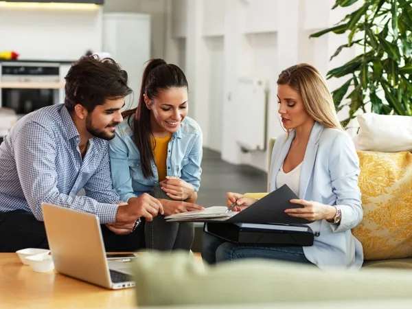 A group of three individuals on a couch, looking at a document.