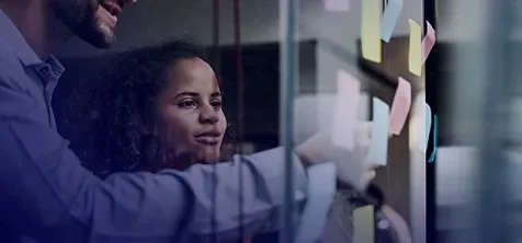 A man and woman pasting sticky notes on a glass wall