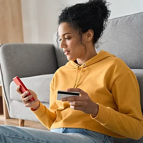 A lady holding a credit card and looking at a mobile phone