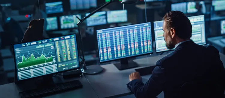 Trader at multiple monitors analyzing stock charts and financial data