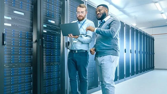 Two people working on laptop inside server room with racks