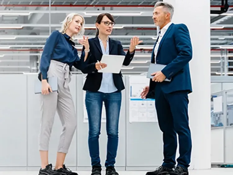 Three professionals discussing with tablet together in modern industrial office setting