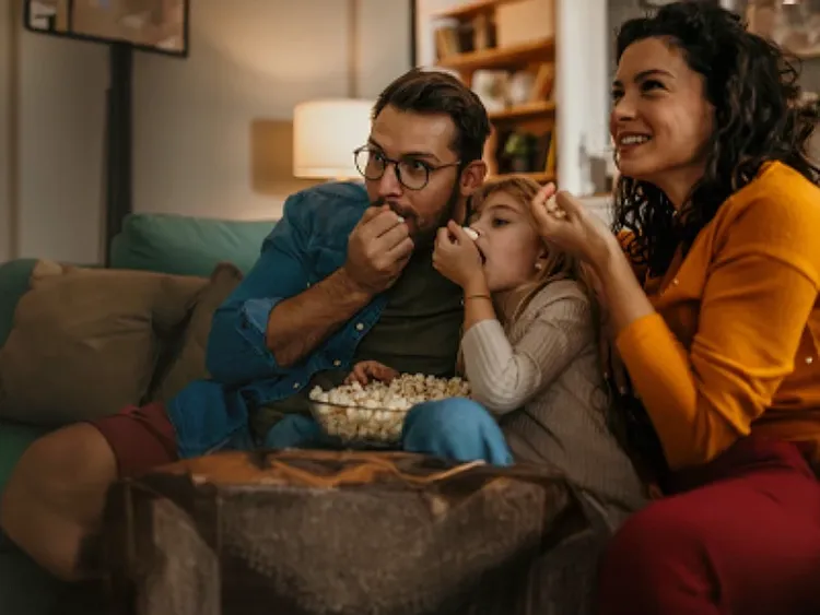 A cheerful family enjoying a movie on TV while sharing popcorn