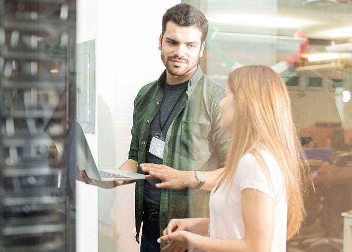 Two business people standing in server room with laptop and discussing