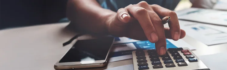 A person engaged in calculating business expenses with a calculator, papers, and a pen on the table.