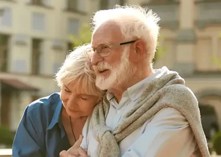 An elderly woman leaning against an elderly man