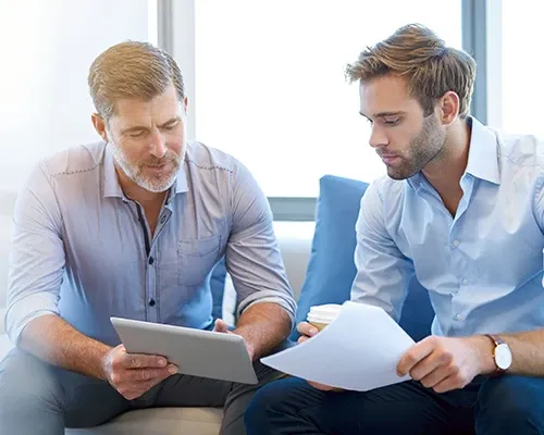 a man holing a tab is discussing with a man holding a paper