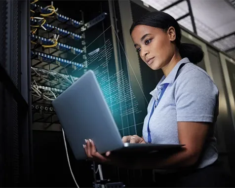 A woman working on a laptop in a server room