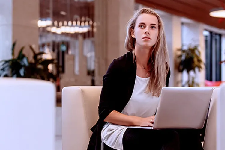 A woman sitting with an open laptop in a hotel lobby