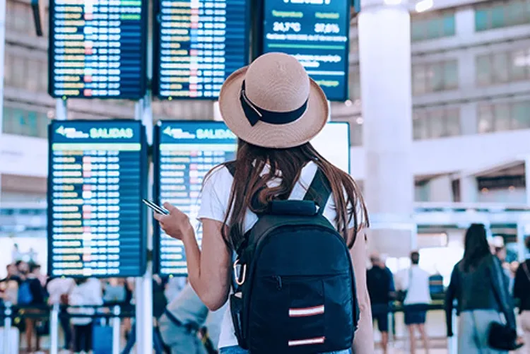 A woman wearing a hat and a backpack looking at flight schedule displays at an airport