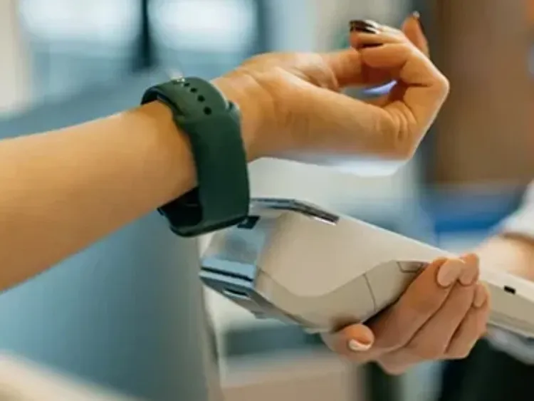 Hand holding a payment terminal while another makes a wearable tap