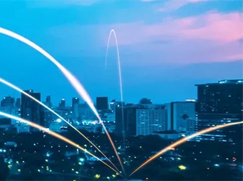 City skyline illuminated at night, featuring vibrant light trails weaving through the buildings.