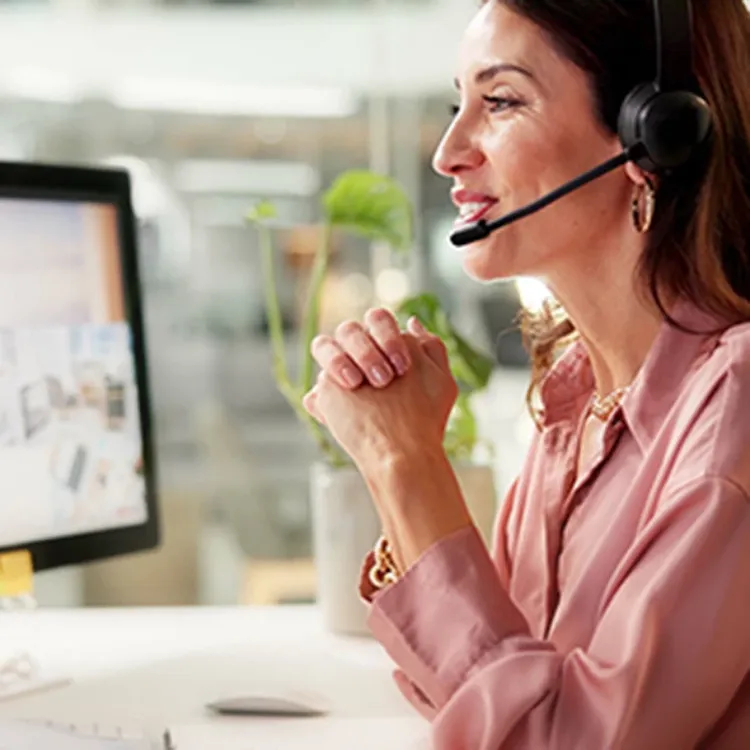 A female helpdesk worker wearing a headset talking to a customer while looking into a monitor at work