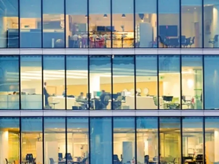 Office building windows showing multiple brightly lit workspaces inside