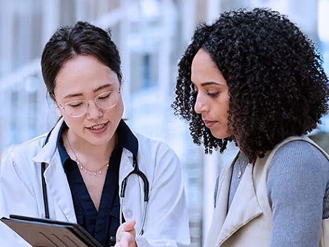 Healthcare professional showing tablet information to person in modern hallway