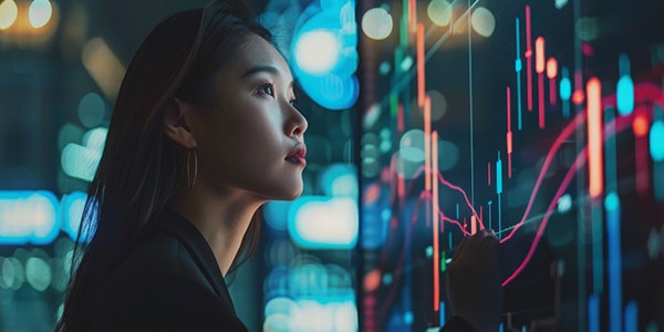 A woman studies a stock market graph on a screen.