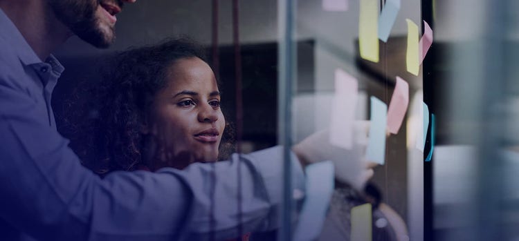 A man and woman pasting sticky notes on a glass wall