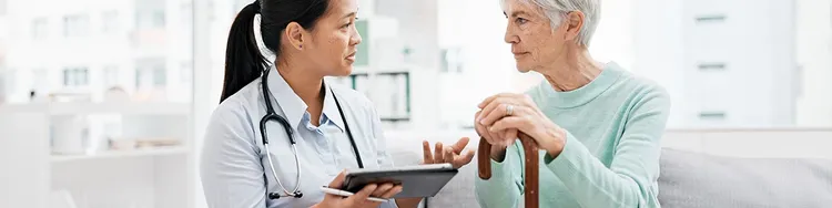 A doctor holding a tablet talks to an elderly patient with in room.