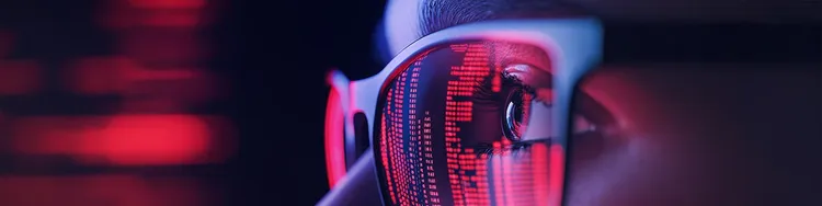 A close-up of an individual wearing glasses that emit a soft red glow, highlighting their facial features.