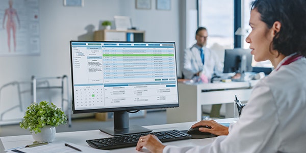 A woman in a white lab coat is focused on her work while using a computer in a laboratory.