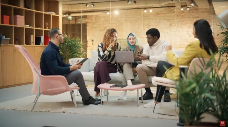 A group of colleagues in a casual setting having a conversation and looking at laptop screen.