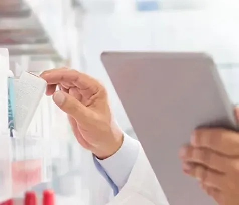 A pharma professional holding a tablet with one hand and picking up a healthcare product off the shelf
