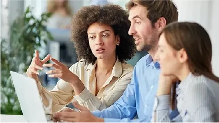 Three colleagues looking at a laptop screen and discussing something