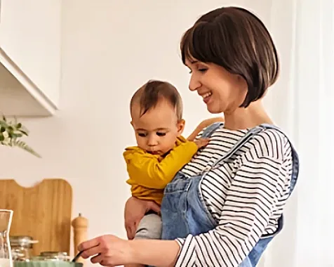 A woman holding a baby & stirring food in a bowl