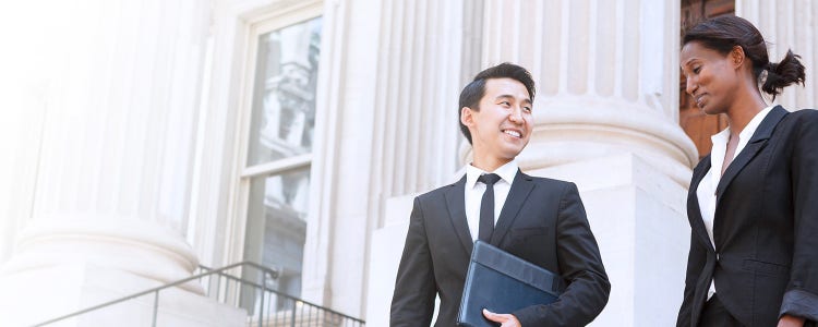 Two individuals in business attire standing in front of a modern office building, discussing work matters.