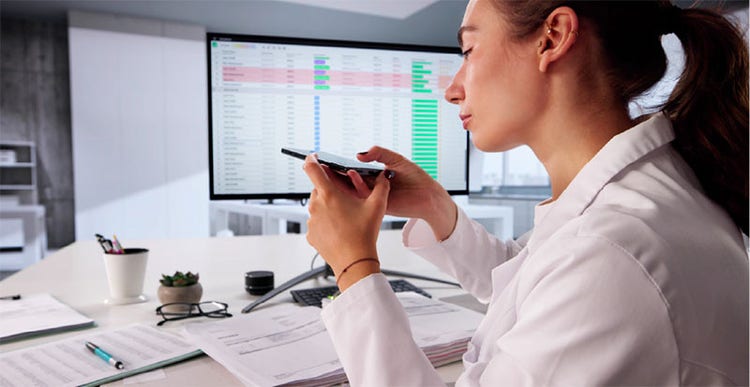 A woman in a lab coat is focused on her cell phone while standing in a laboratory setting.