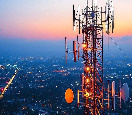 Sunset casts a warm glow on cell towers rising above a city, highlighting the importance of telecom connectivity