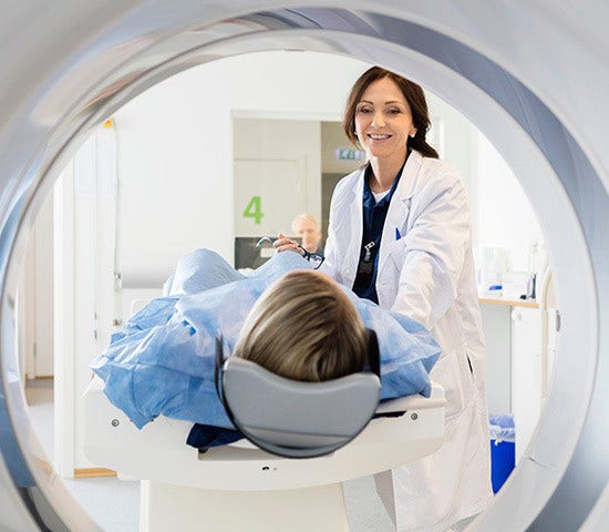 A woman wearing a hospital gown is positioned in an MRI machine, indicating a healthcare examination in progress