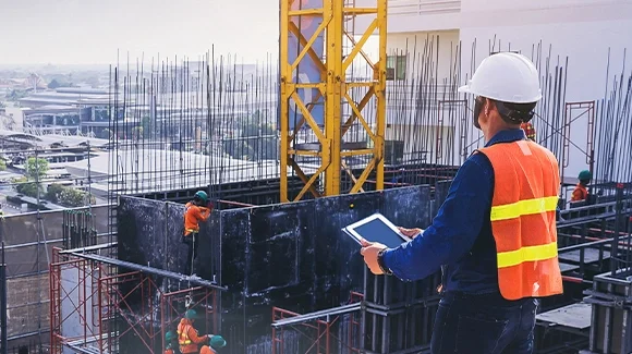 Construction site supervisor using a tablet to monitor building progress on a high-rise construction project.