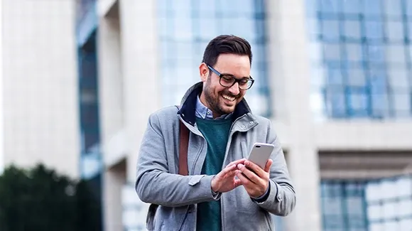 Person using a smartphone outside a modern office building, demonstrating mobile business technology and digital connectivity.